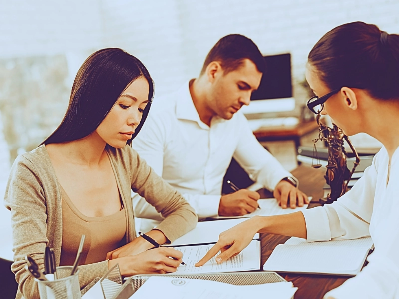 Woman signing legal documents with lawyer's assistance.